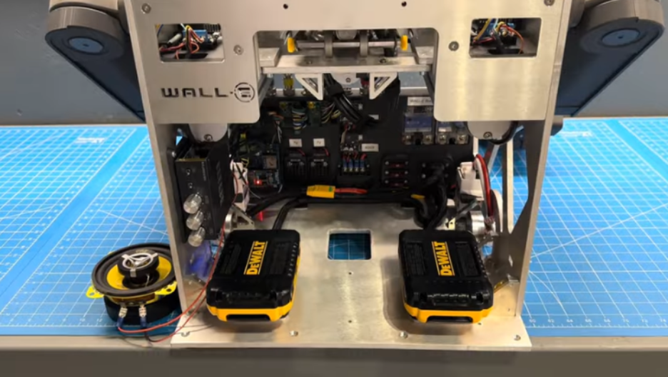 Rear view of Wall-E's open aluminum chassis showing the two-battery setup, speaker, fuses, and wiring with the arms mounted on each side
